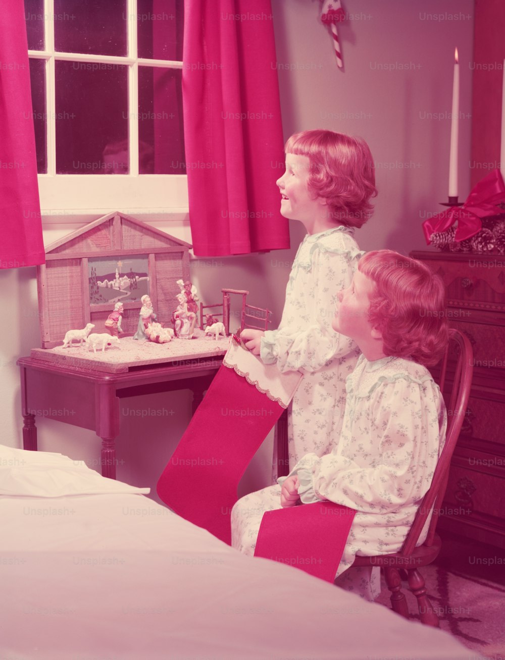 미국 - 1950년대경: 크리스마스 스타킹을 들고 침실 창 밖을 내다보는 쌍둥이 소녀, 야간 테이블의 탄생 장면.