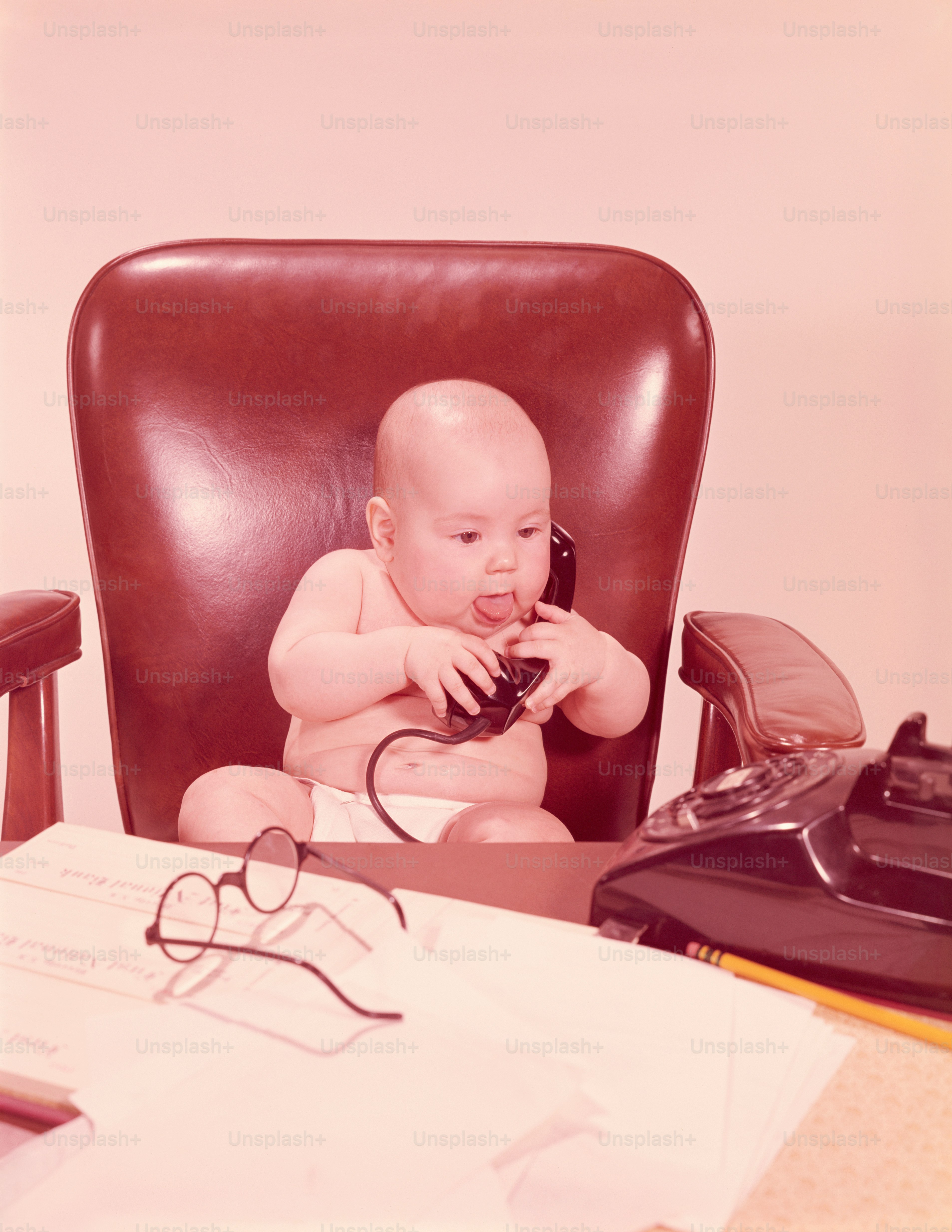 ESTADOS UNIDOS - POR VOLTA DE 1950: Bebê sentado na mesa do escritório, segurando o telefone.