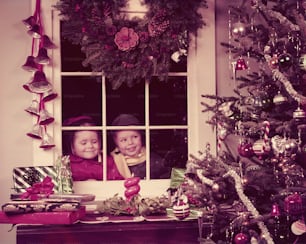 UNITED STATES - CIRCA 1950s:  Boy and girl peeking in window, looking at decorated Christmas tree.