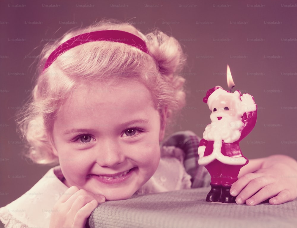 UNITED STATES - CIRCA 1950s:  Girl holing Father Christmas candle, smiling, portrait.