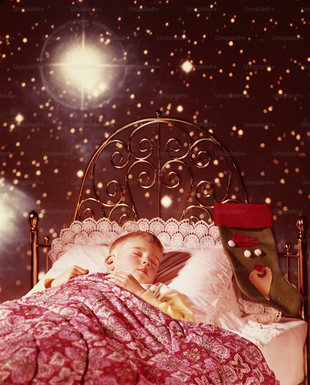 UNITED STATES - CIRCA 1960s:  Little boy sleeping in brass bed with Christmas stocking and starry dream images.