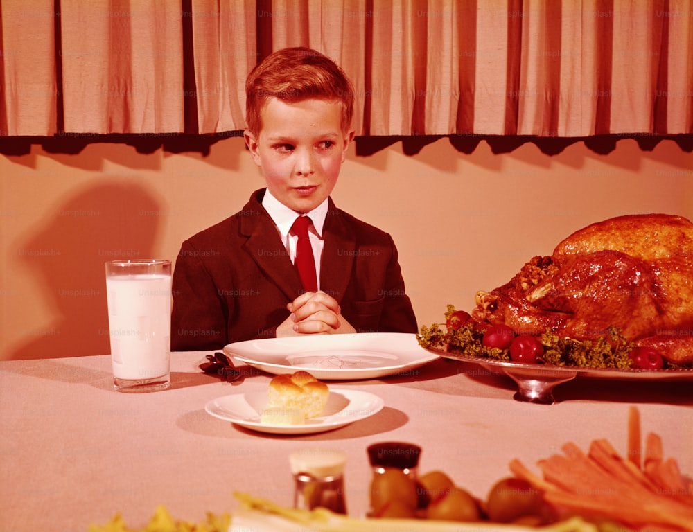 UNITED STATES - CIRCA 1960s:  Boy sitting  at table with hands folded for grace prayer, looking at roast turkey.