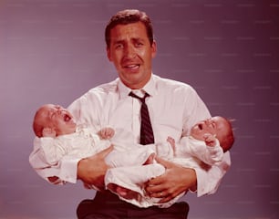 미국 - 1950년대경: 울고 있는 쌍둥이 아기를 팔에 안고 괴로워 보이는 아버지.