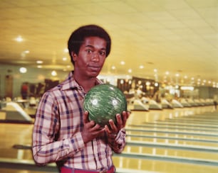 STATI UNITI - CIRCA 1970: Uomo che tiene palla da bowling marmorizzata verde in pista da bowling, corsie sullo sfondo.