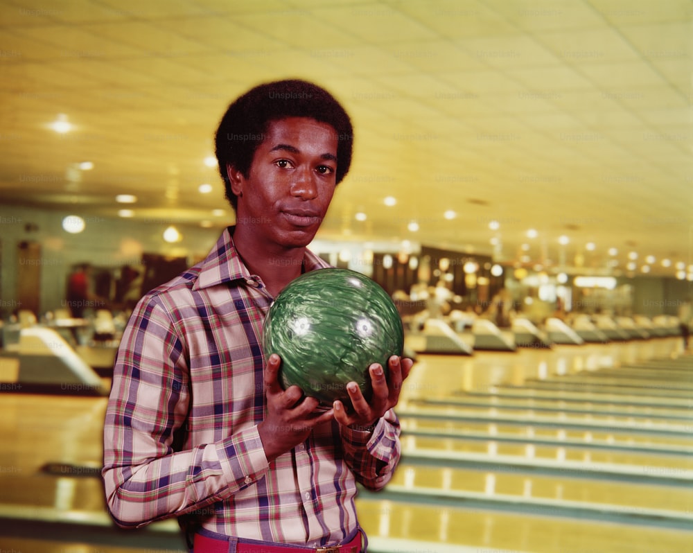 UNITED STATES - CIRCA 1970s:  Man holding green marbleized bowling ball in bowling alley, lanes in background.