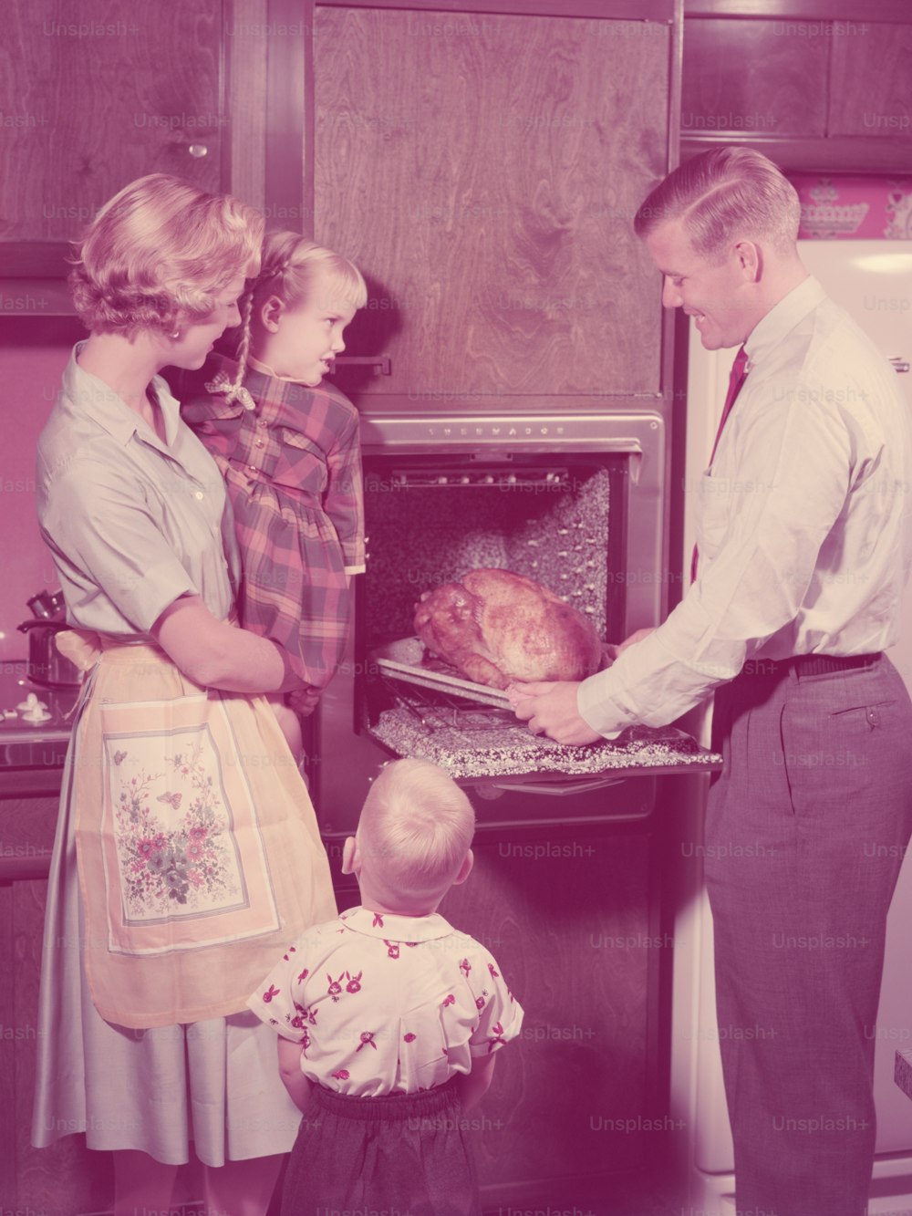 미국 - 1950년대경: 부엌에 있는 가족, 오븐에서 구운 칠면조를 꺼내는 아버지, 어머니와 아이들이 지켜보고 있습니다.