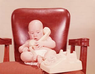 ESTADOS UNIDOS - CIRCA 1950s: Bebé sentado en el escritorio de la oficina, sosteniendo el teléfono.