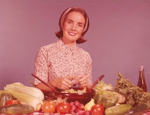 STATI UNITI - CIRCA 1960: Donna al bancone della cucina, lanciando verdure per insalata.