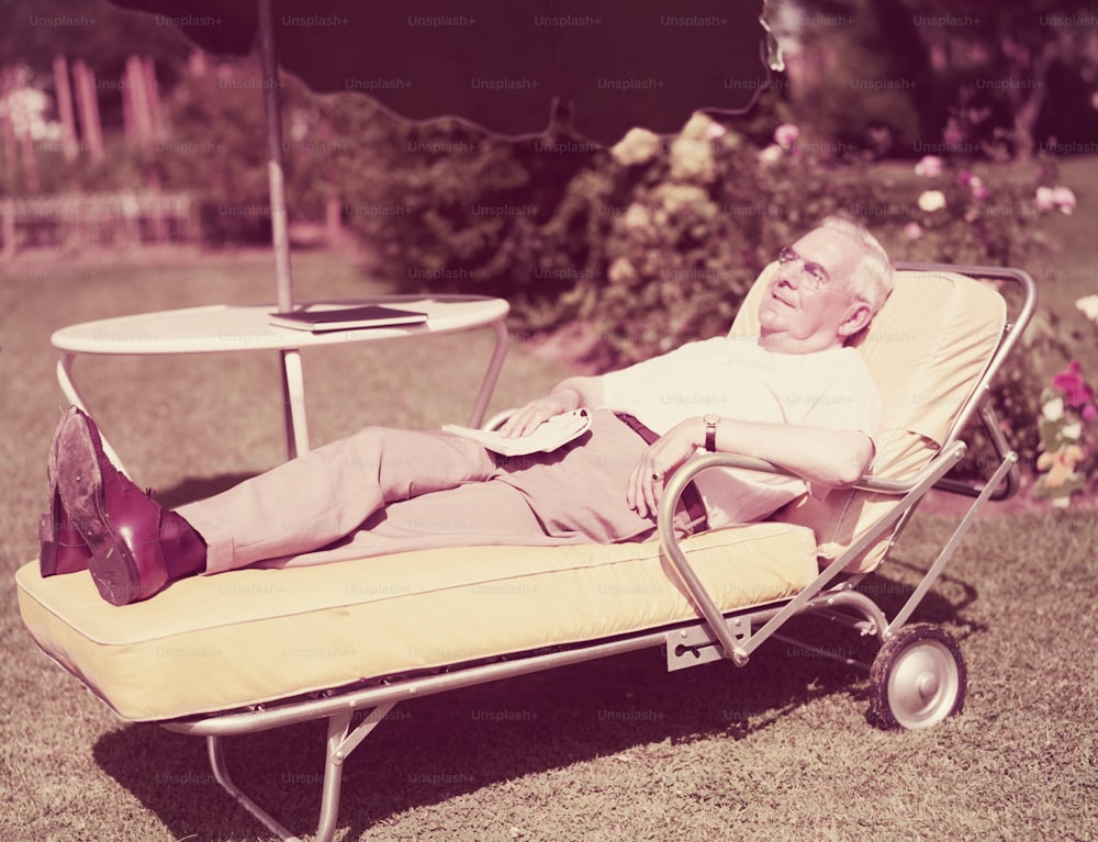 UNITED STATES - CIRCA 1950s:  Elderly man relaxing on sun lounger in backyard.