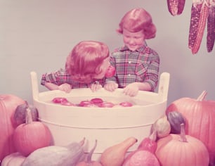 미국 - 1950년대경: 파티에서 사과를 먹기 위해 밥을 먹는 쌍둥이 빨간 머리 소녀.