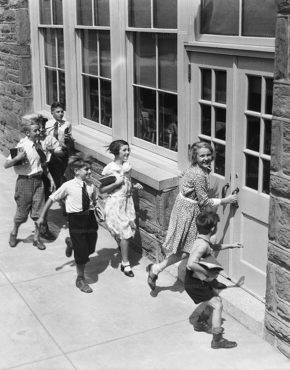 UNITED STATES - CIRCA 1930s:  Seven children carrying books, about to enter schoolhouse.