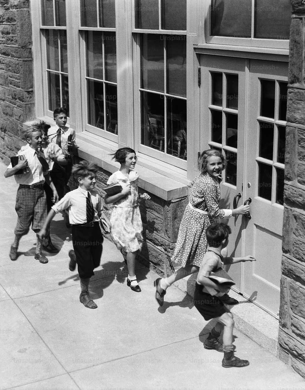 UNITED STATES - CIRCA 1930s:  Seven children carrying books, about to enter schoolhouse.
