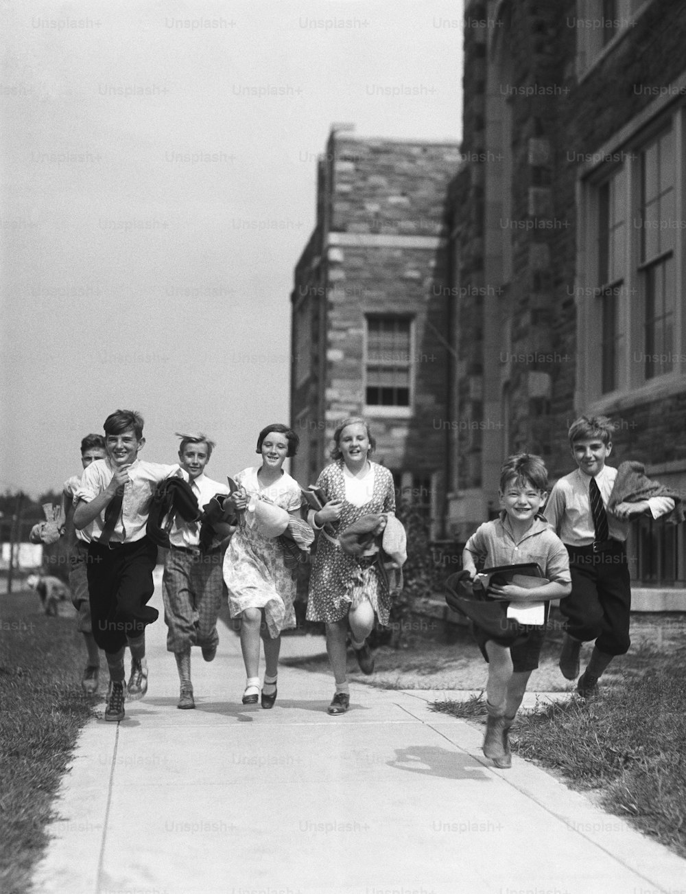 VEREINIGTE STAATEN - CIRCA 1930er Jahre: Sieben Kinder rennen auf dem Bürgersteig vor dem Schulhaus.
