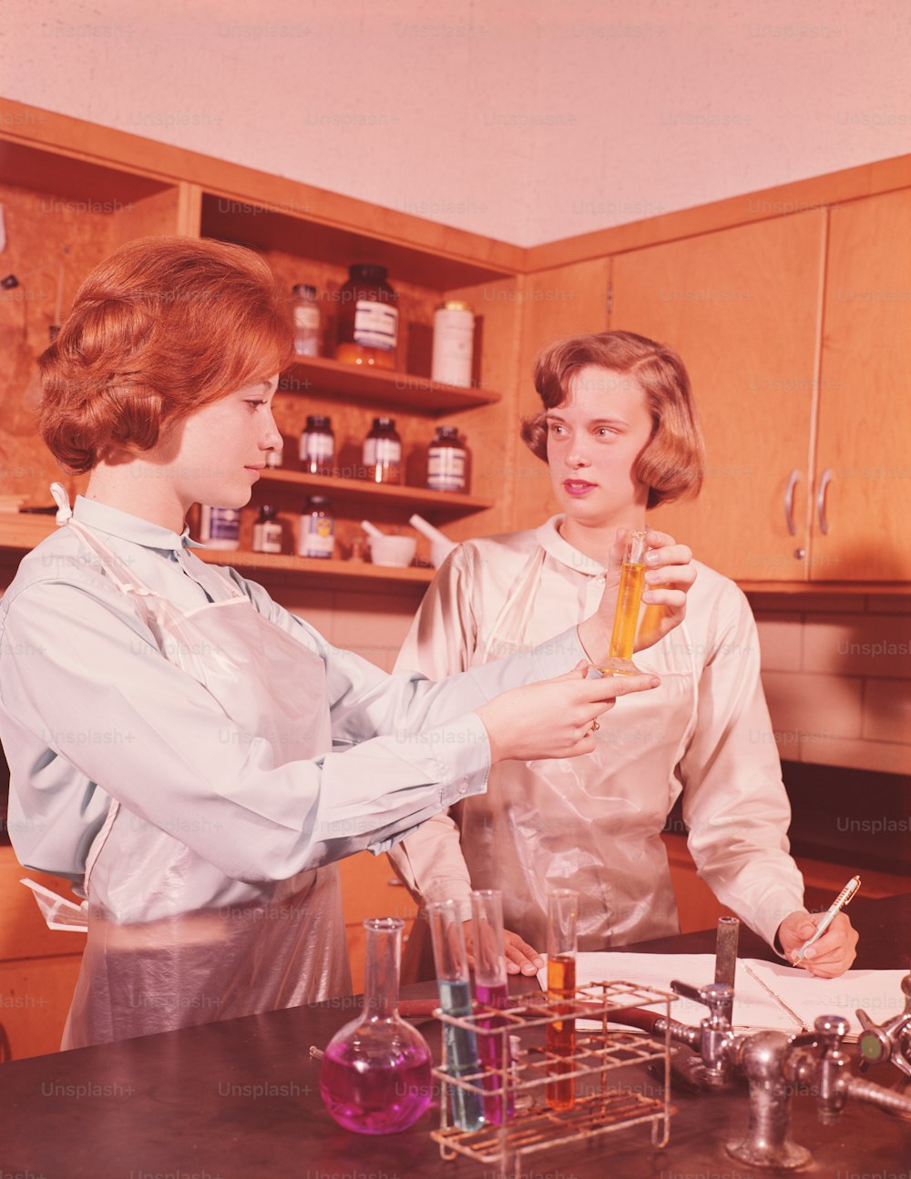 UNITED STATES - CIRCA 1960s:  Two teenage young women in high school chemistry class, conducting chemical experiment.