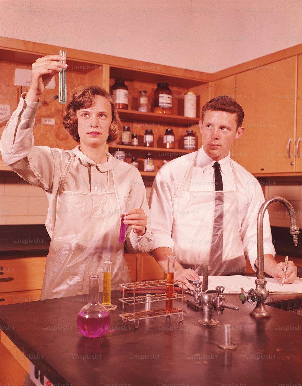 STATI UNITI - CIRCA 1960: Due studenti in un laboratorio di chimica, ragazza che tiene in provetta, ragazzo che prende appunti scientifici.