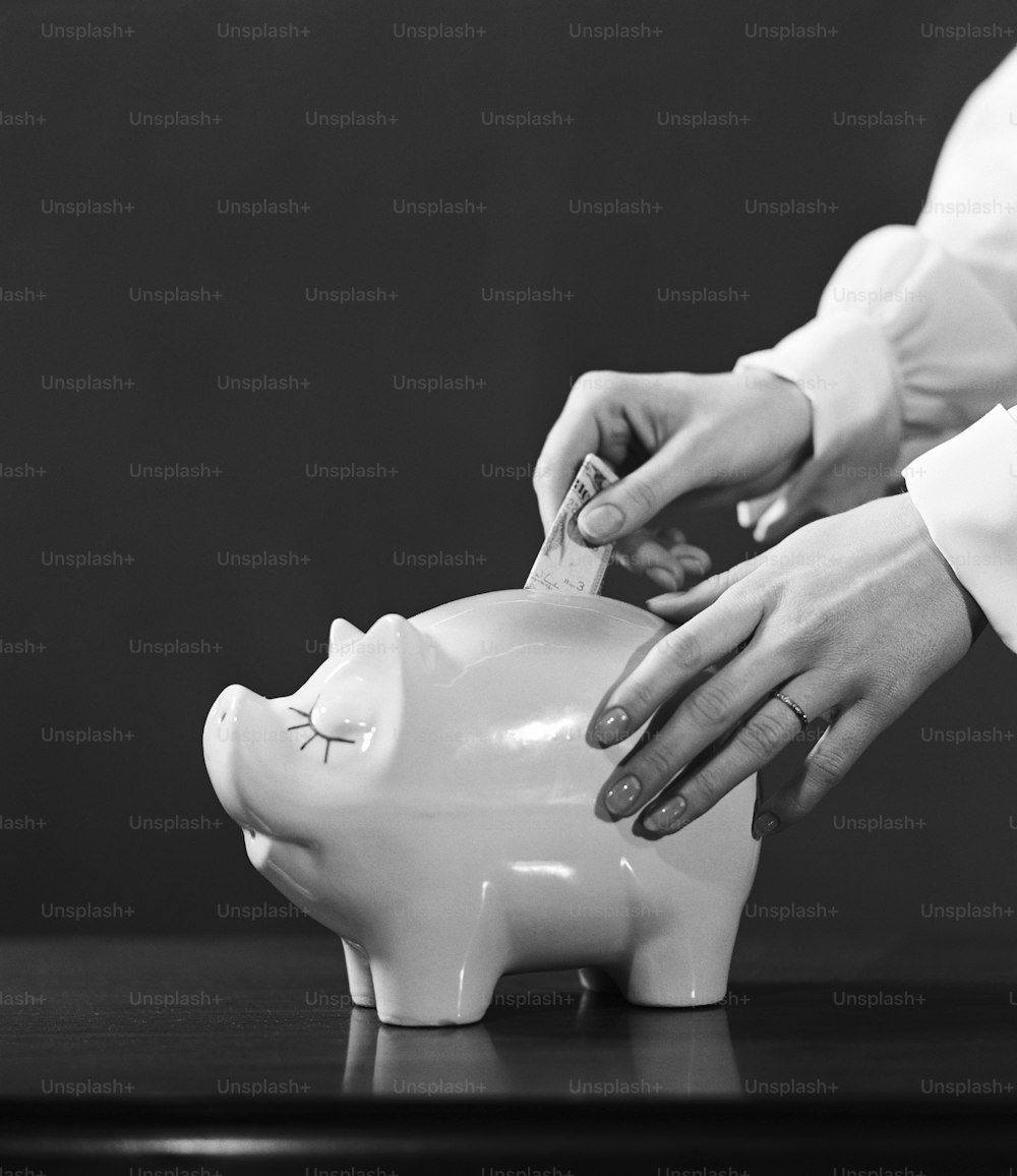 미국 - 1950년대경: 돼지 저금통에 달러 지폐를 넣는 여성의 손.