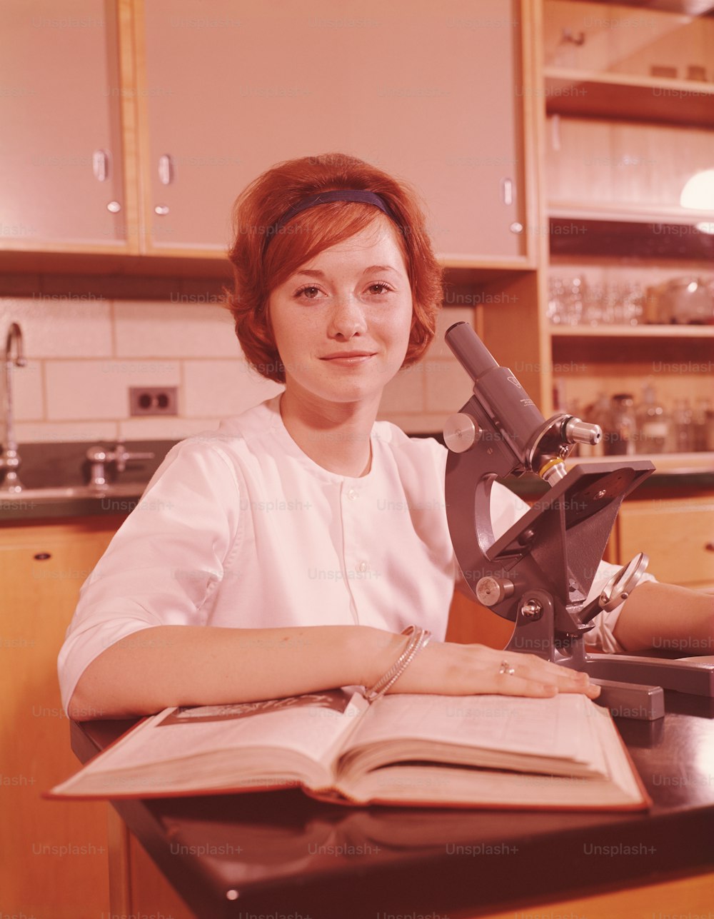 ESTADOS UNIDOS - CIRCA 1960s: Estudiante adolescente sentada junto al microscopio y libro de texto abierto, sonriendo, retrato.