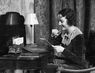 미국 - 1930년대경: 집 책상에 앉아 편지를 쓰는 여성.