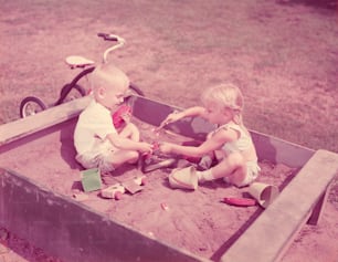 ESTADOS UNIDOS - CIRCA 1950s: Niño y niña jugando en un arenero.