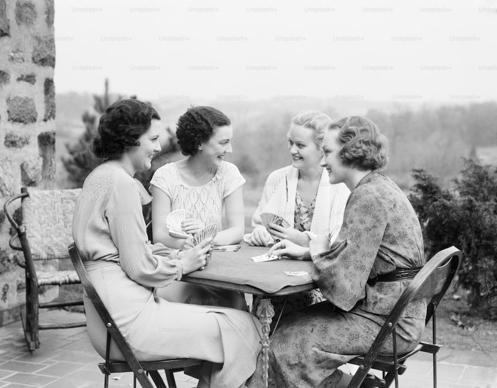 UNITED STATES - CIRCA 1930s:  Four women seated at table on porch of house, playing cards.