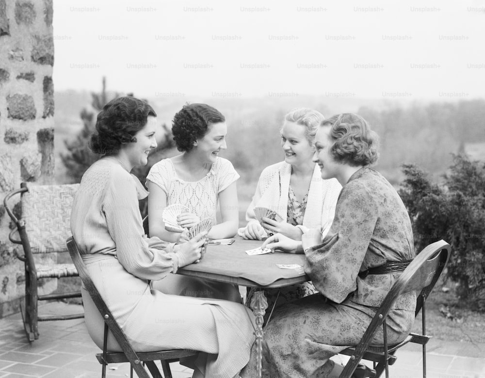 ESTADOS UNIDOS - CIRCA 1930s: Cuatro mujeres sentadas a la mesa en el porche de una casa, jugando a las cartas.