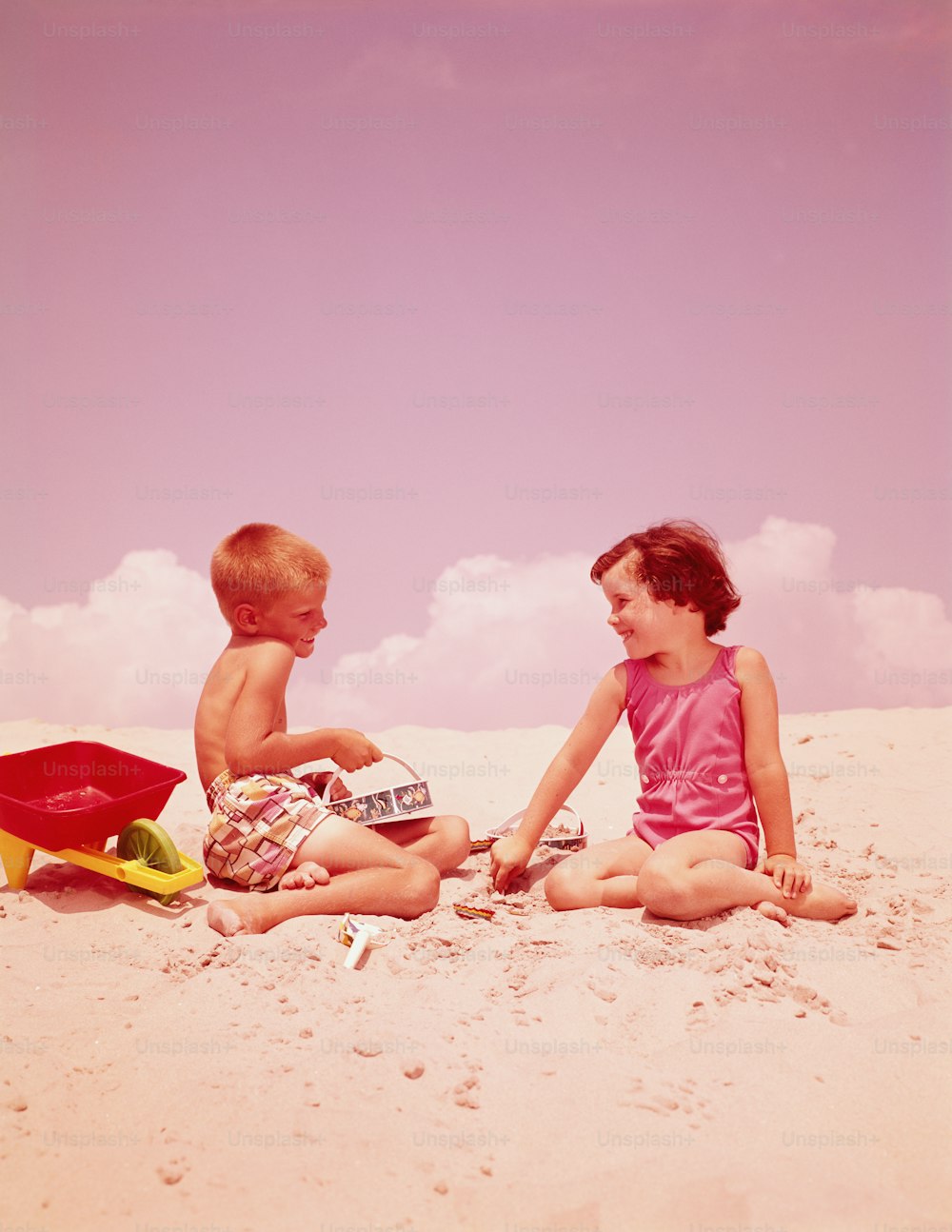 UNITED STATES - CIRCA 1960s:  Young couple sitting in sand, by seashore, flirting.