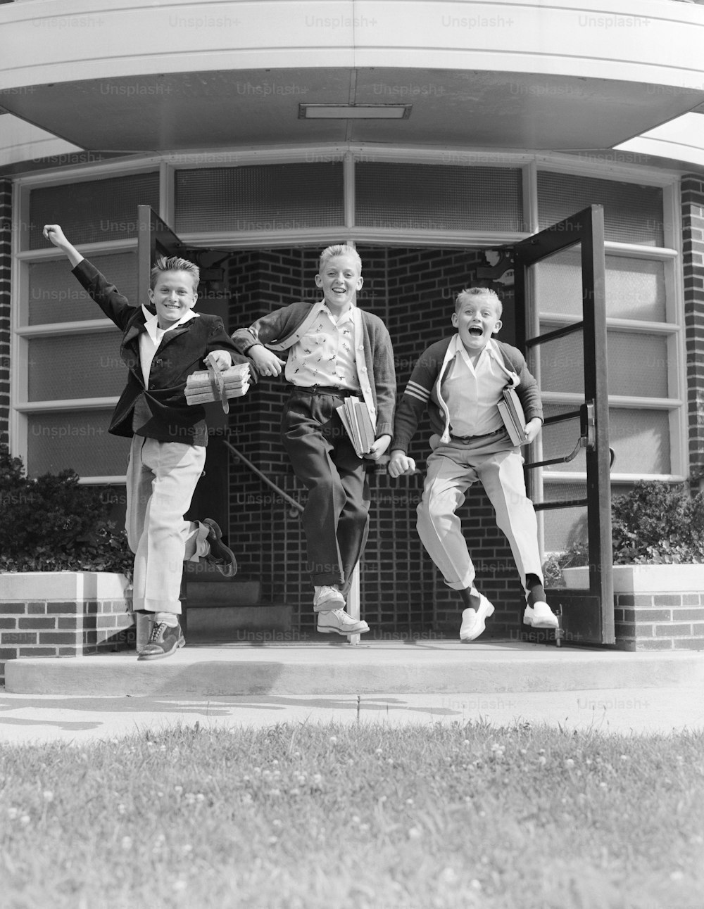 UNITED STATES - CIRCA 1950s:  Three excited boys running out of school.