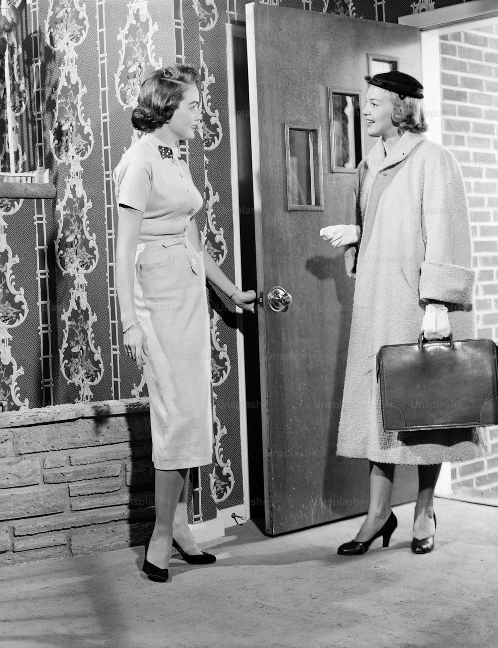 UNITED STATES - CIRCA 1950s:  Woman opening door to saleswoman.