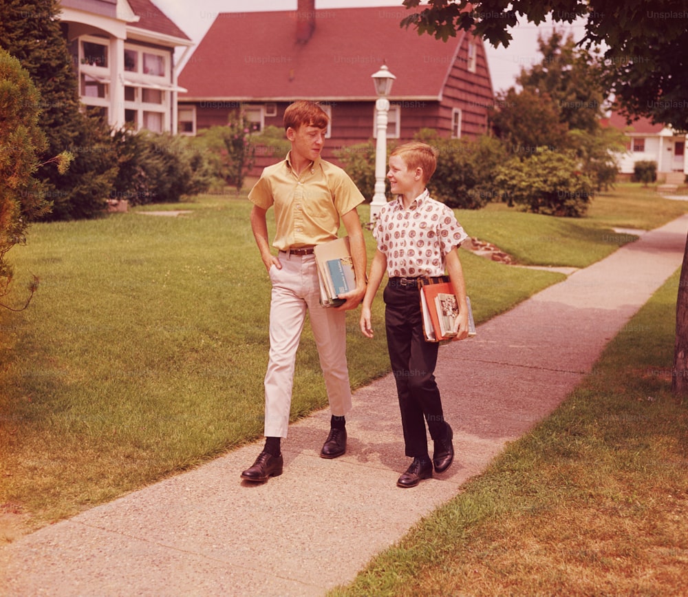 VEREINIGTE STAATEN - CIRCA 1960er Jahre: Zwei Jungen, die die Straße entlang gehen, reden, Schulbücher tragend.
