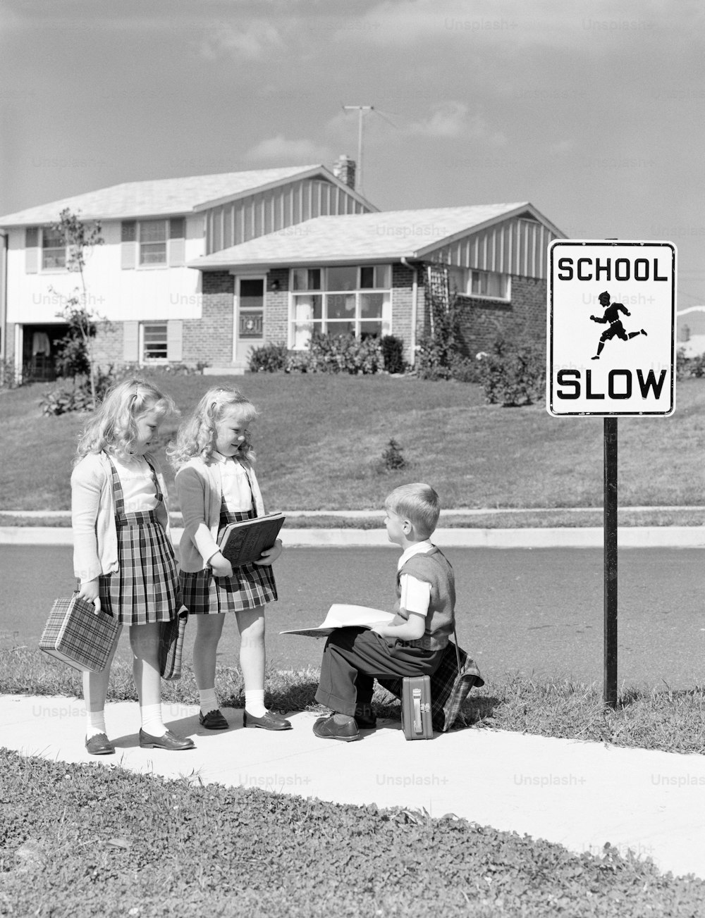 UNITED STATES - CIRCA 1950s:  Two girls walking to school, boy sitting on lunchbox.