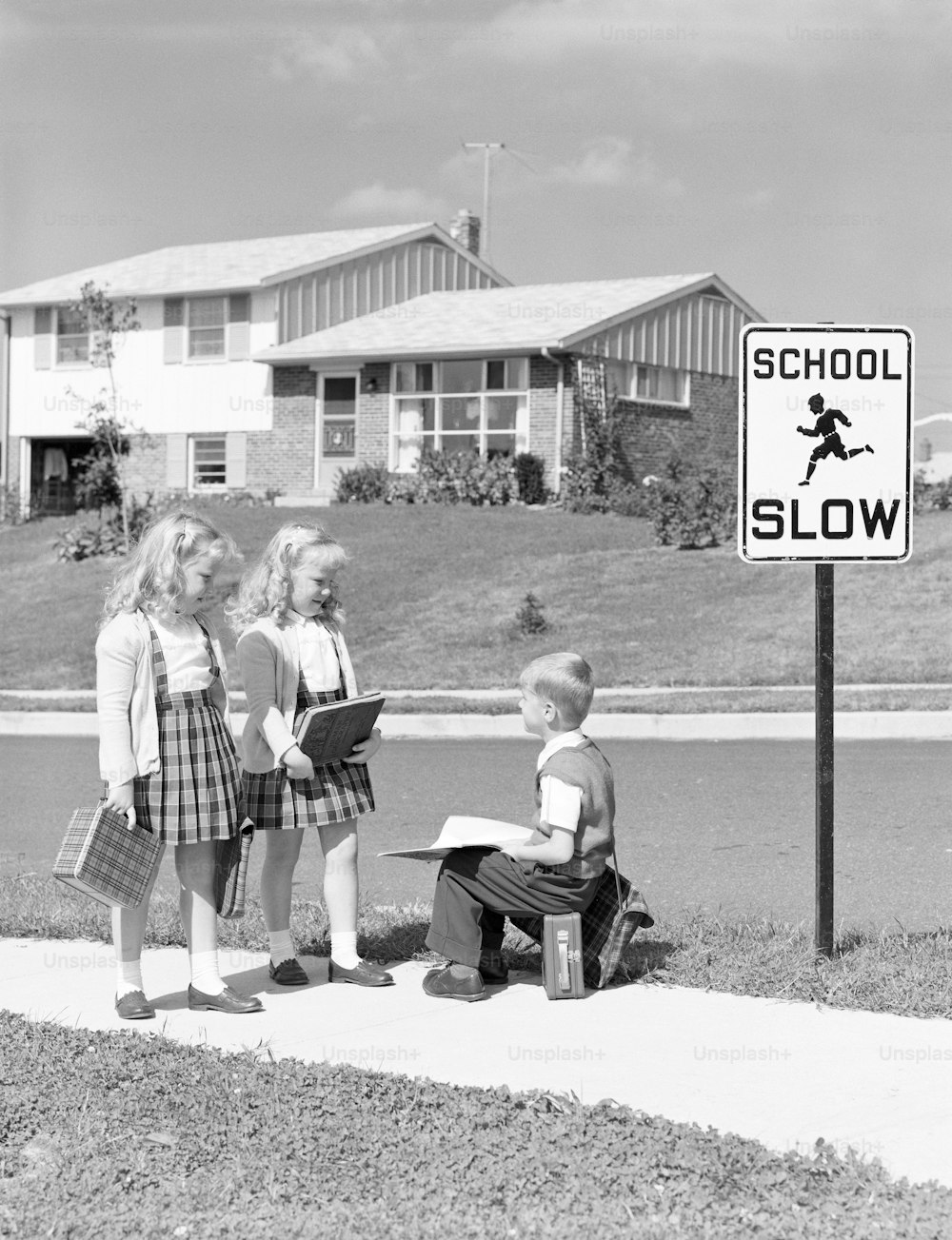 UNITED STATES - CIRCA 1950s:  Two girls walking to school, boy sitting on lunchbox.