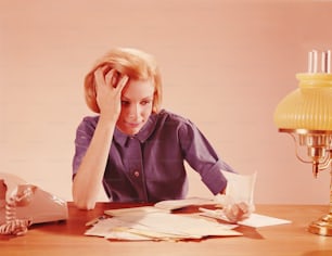UNITED STATES - CIRCA 1960s:  Frustrated woman at home desk, working on home finances, crunching bills in fist.
