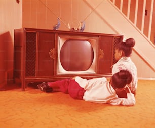 1970年代頃のアメリカ:リビングルームの床でテレビを見ている2人の女の子。