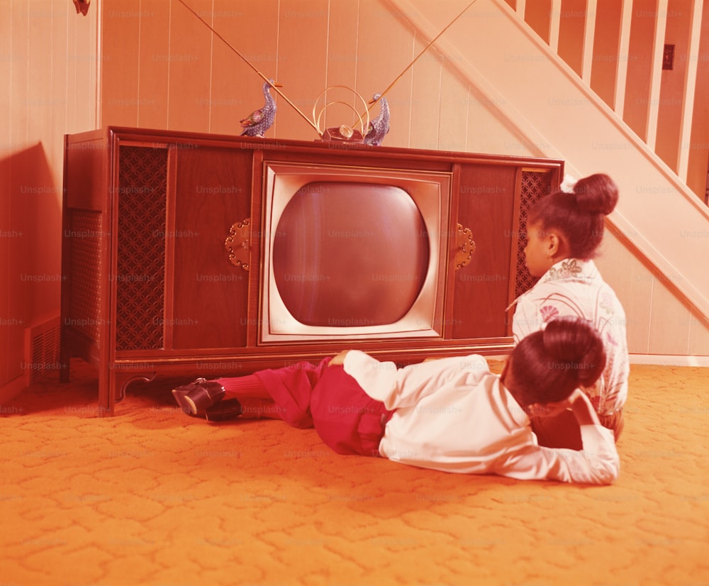STATI UNITI - 1970 CIRCA: Due ragazze sul pavimento del soggiorno, guardando la televisione.