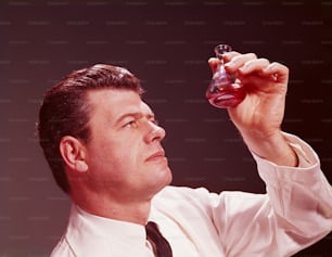 ESTADOS UNIDOS - CIRCA 1950s: Técnico científico observando un líquido coloreado en un vaso de precipitados.