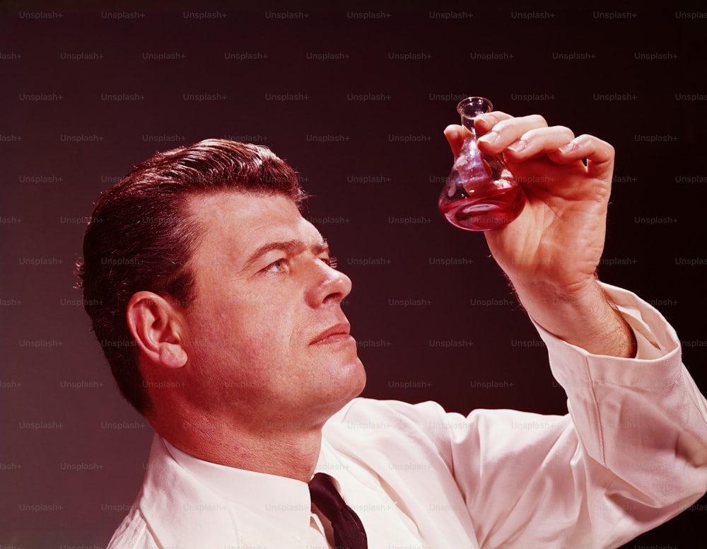 UNITED STATES - CIRCA 1950s:  Scientific technician looking at coloured liquid in beaker.