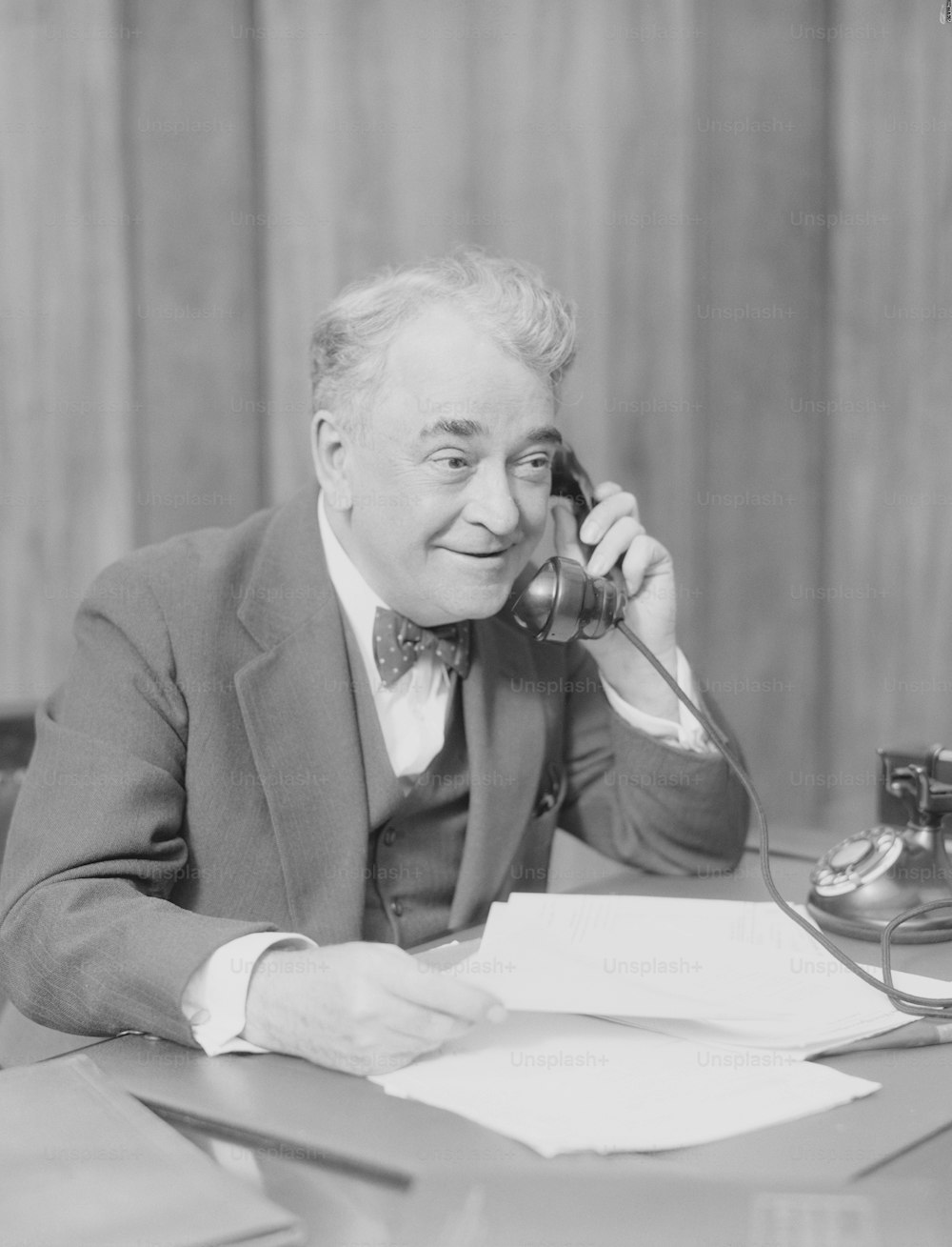 UNITED STATES - CIRCA 1930s:  Elderly businessman, sitting at desk, talking on telephone.
