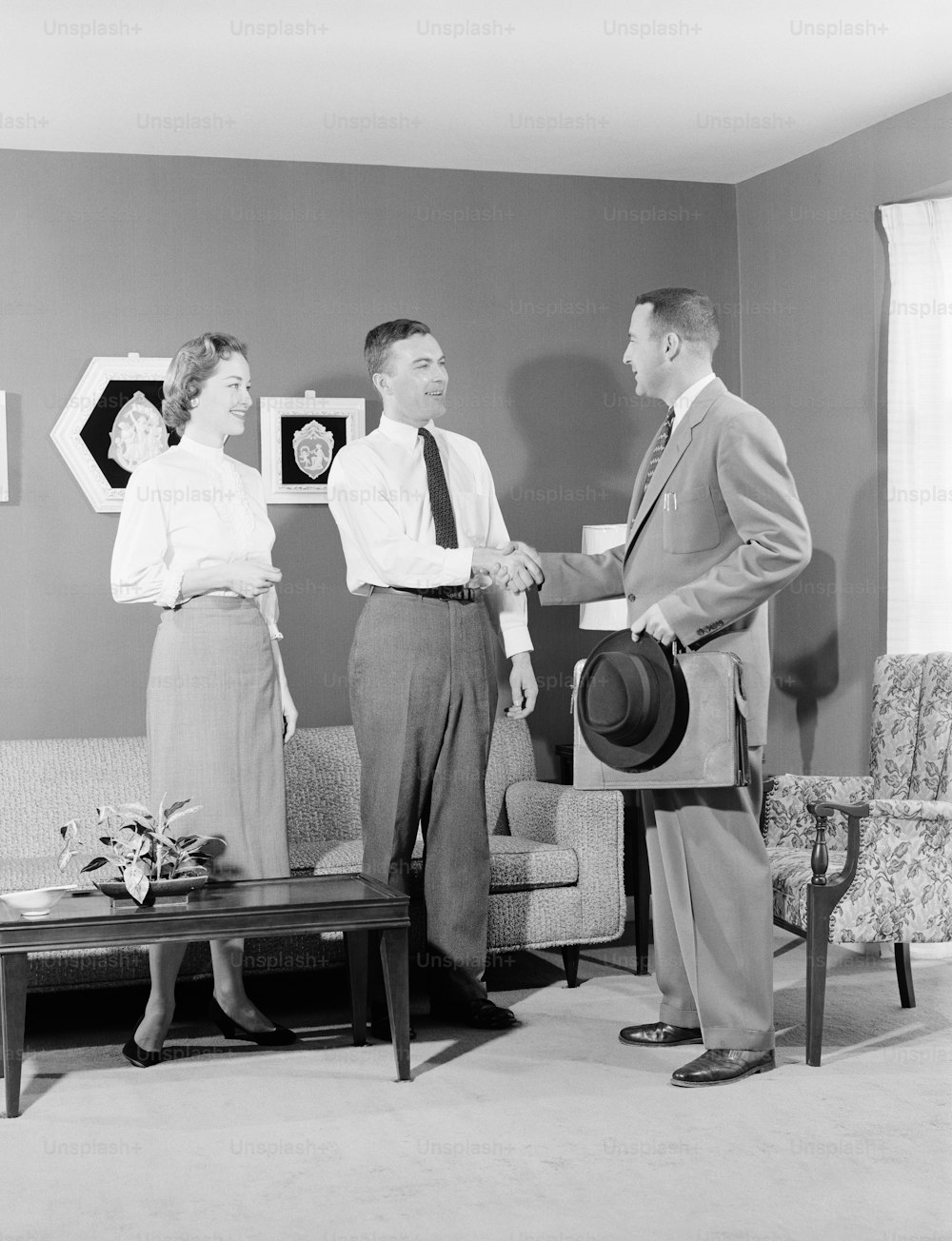 UNITED STATES - CIRCA 1950s:  Couple with salesman in home, men shaking hands.