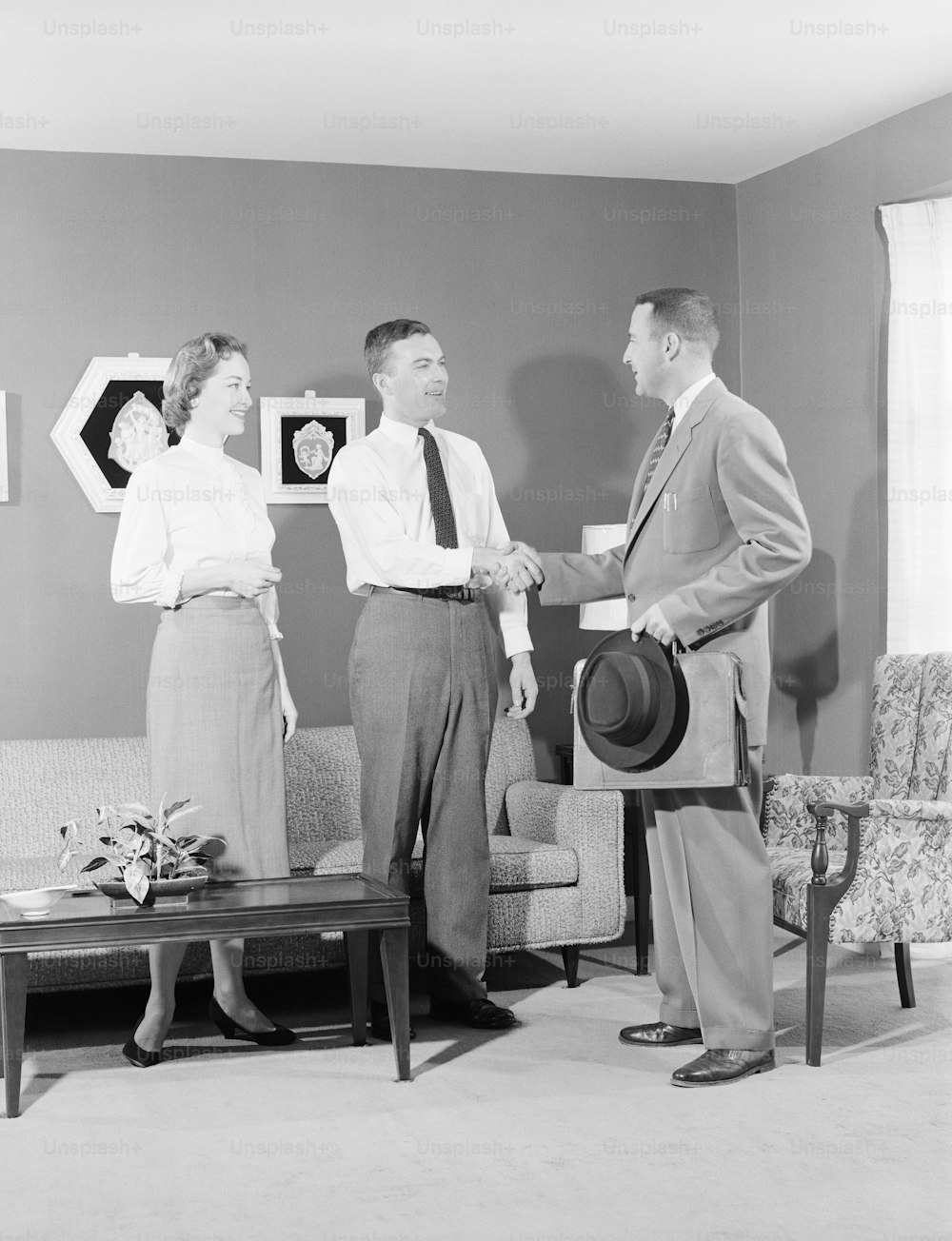 UNITED STATES - CIRCA 1950s:  Couple with salesman in home, men shaking hands.