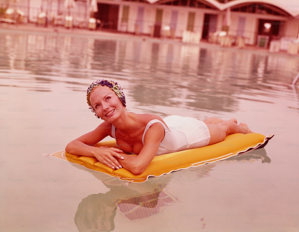 VEREINIGTE STAATEN - CIRCA 1970er Jahre: Frau im Schwimmbad, die auf einem Schlauchboot liegt, Badekappe trägt und lächelt.