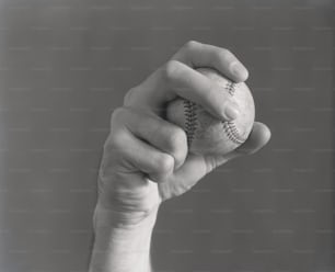 ESTADOS UNIDOS - CIRCA 1930s: Mano de hombre sosteniendo pelota de béisbol en forma de lanzamiento.