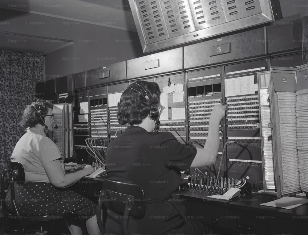 UNITED STATES - CIRCA 1950s:  Two women wearing headsets, working on telephone switchboard.