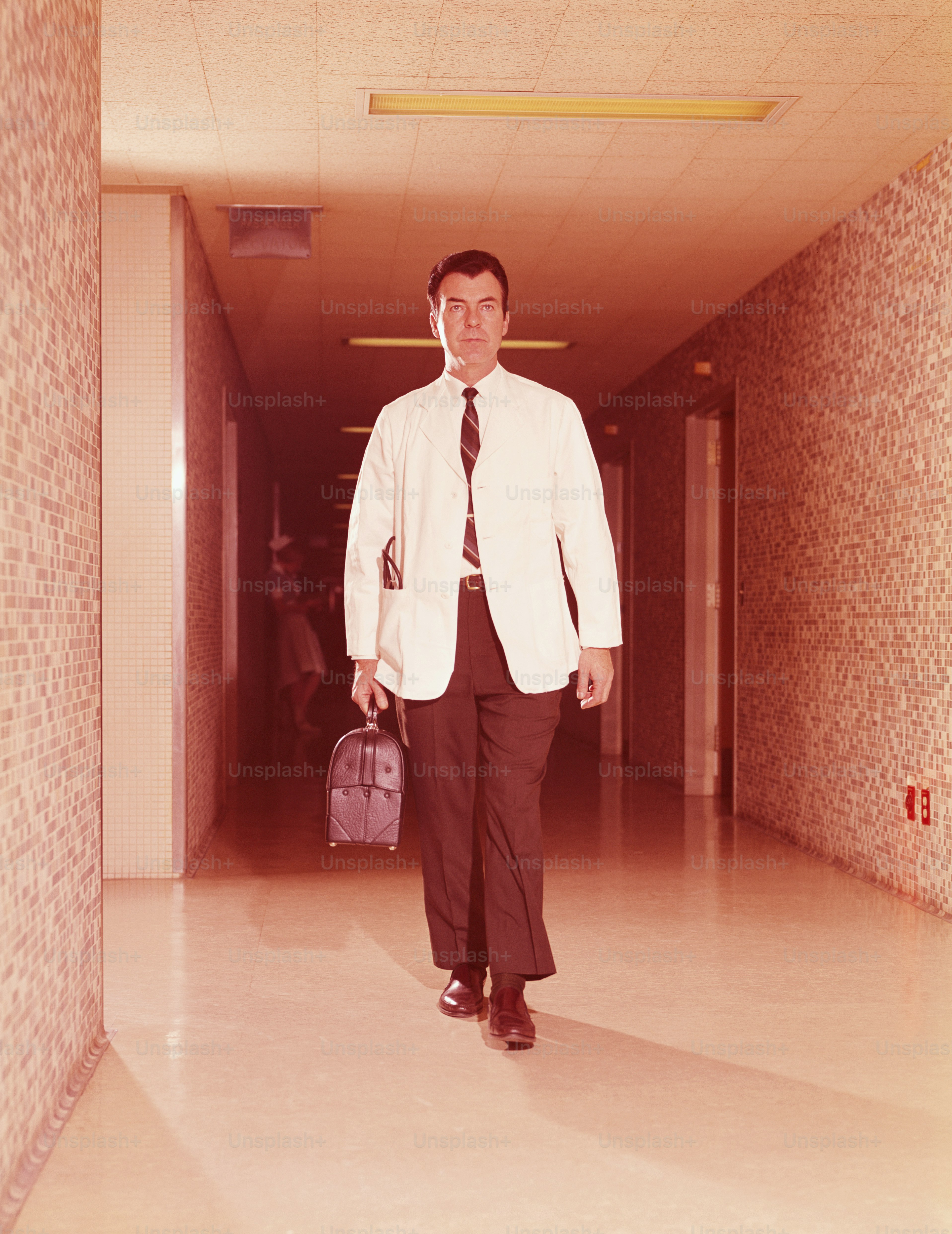 ESTADOS UNIDOS - CIRCA 1960s: Médico caminando por el pasillo del hospital, cargando una bolsa.