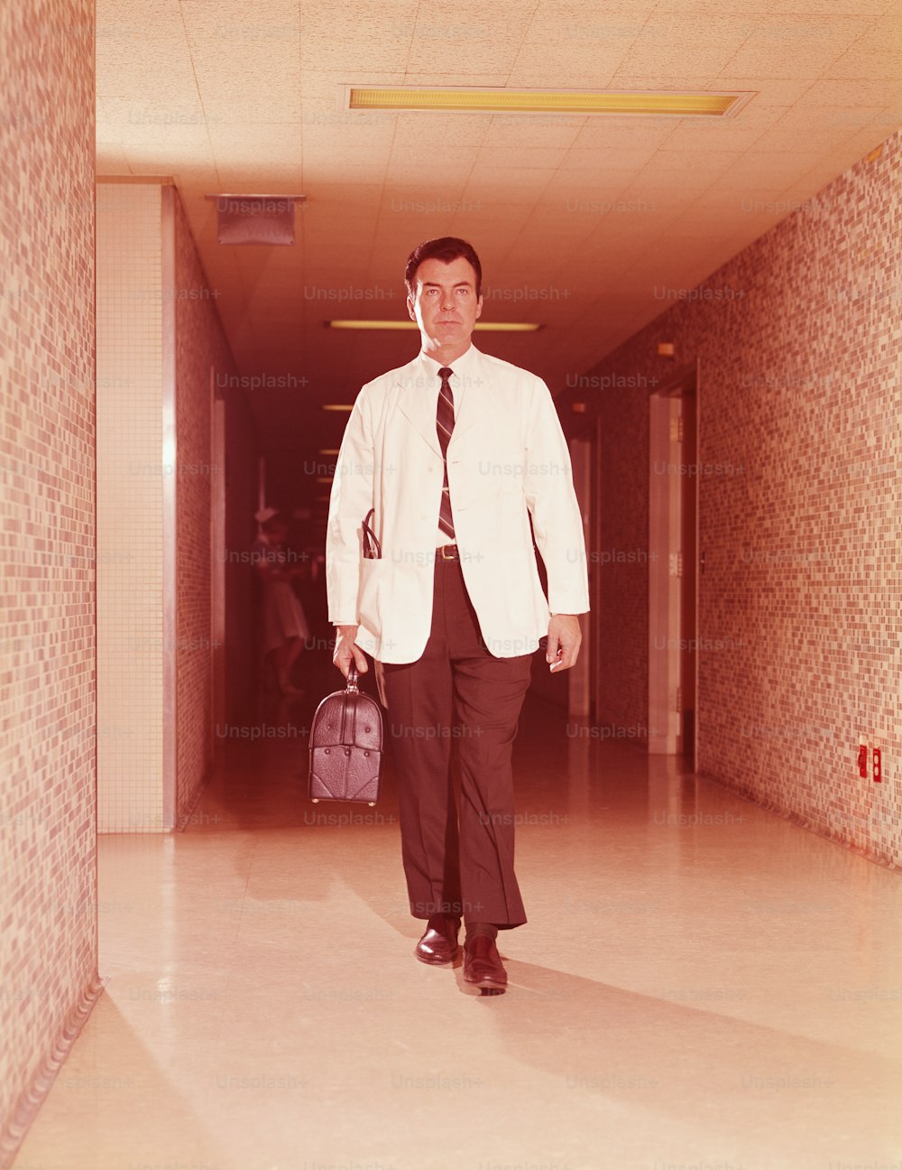 UNITED STATES - CIRCA 1960s:  Doctor walking along hospital corridor, carrying bag.