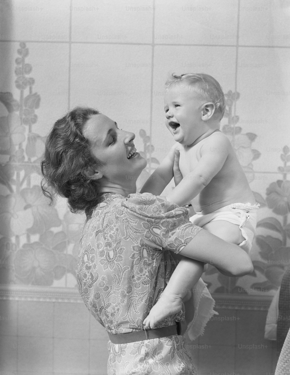 UNITED STATES - CIRCA 1940s:  Smiling mother lifting her crying baby son, looking up at him.