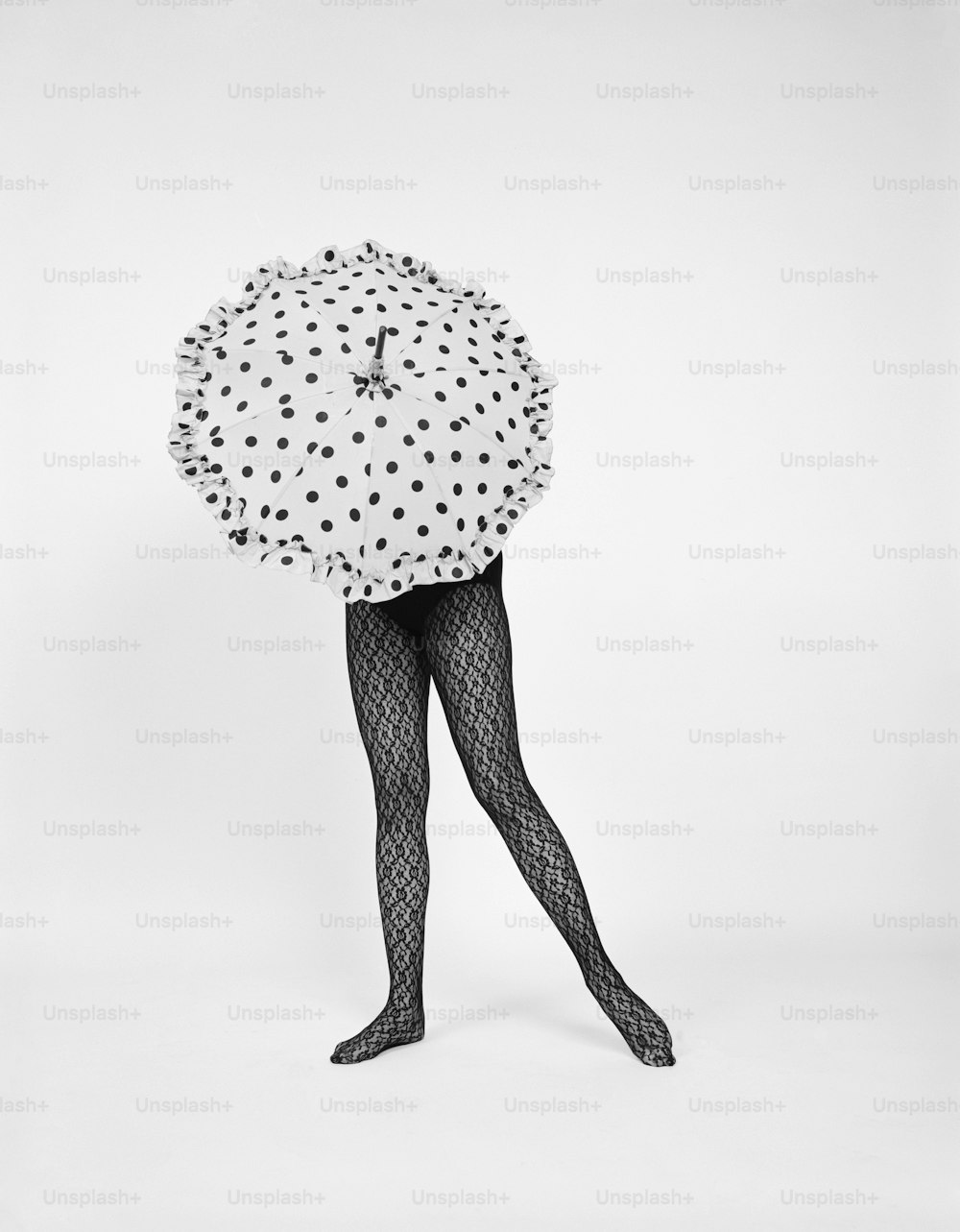 UNITED STATES - CIRCA 1960s: Woman wearing stockings and holding polka dot umbrella.