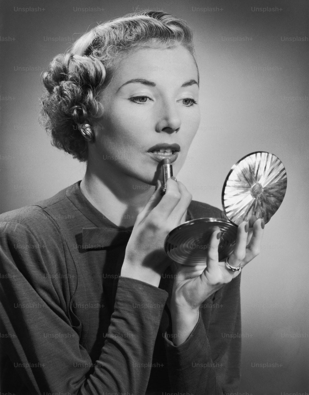 Una mujer aplicando su lápiz labial con la ayuda de un polvo compacto, alrededor de 1955.