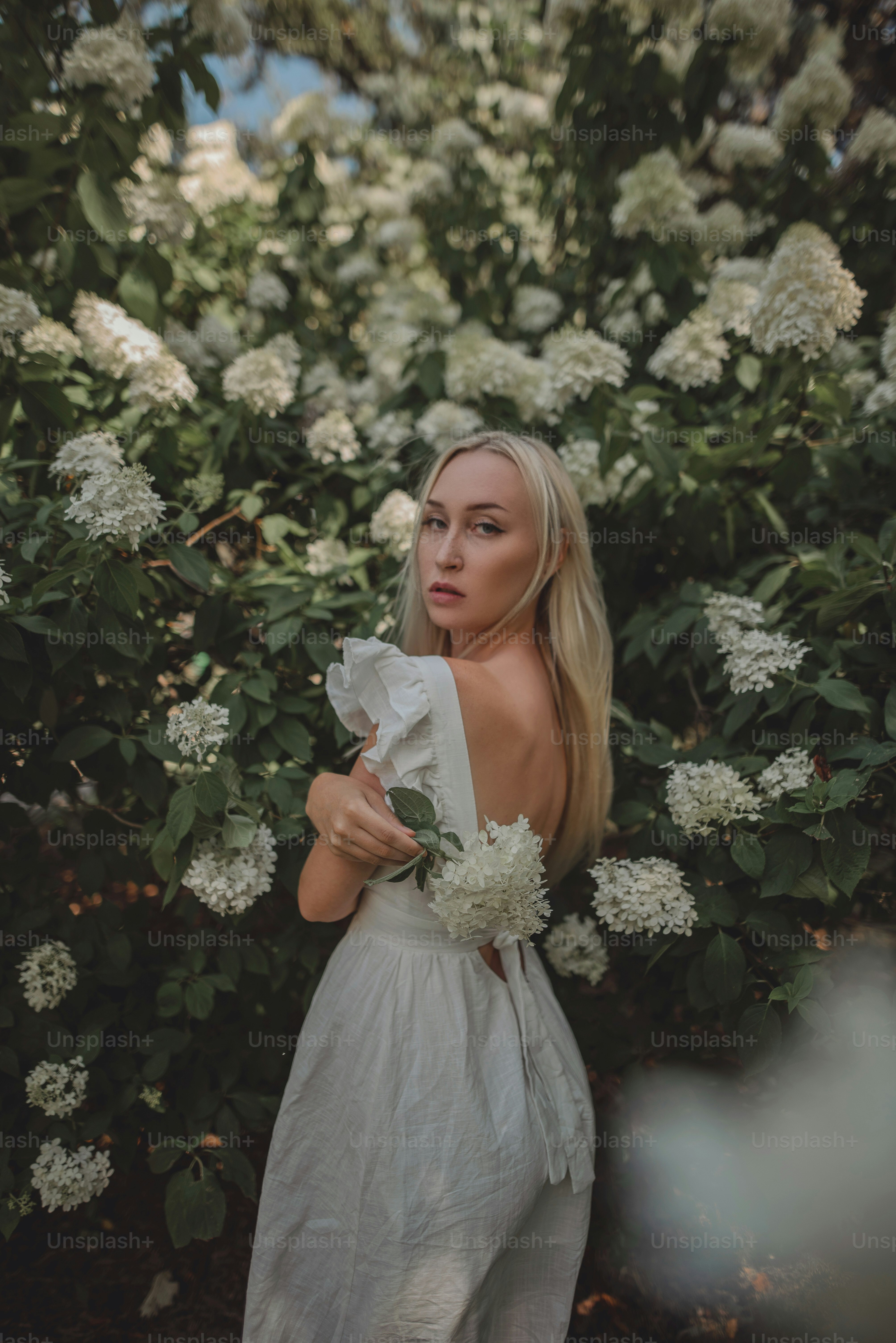 Une femme debout devant un buisson avec des fleurs blanches