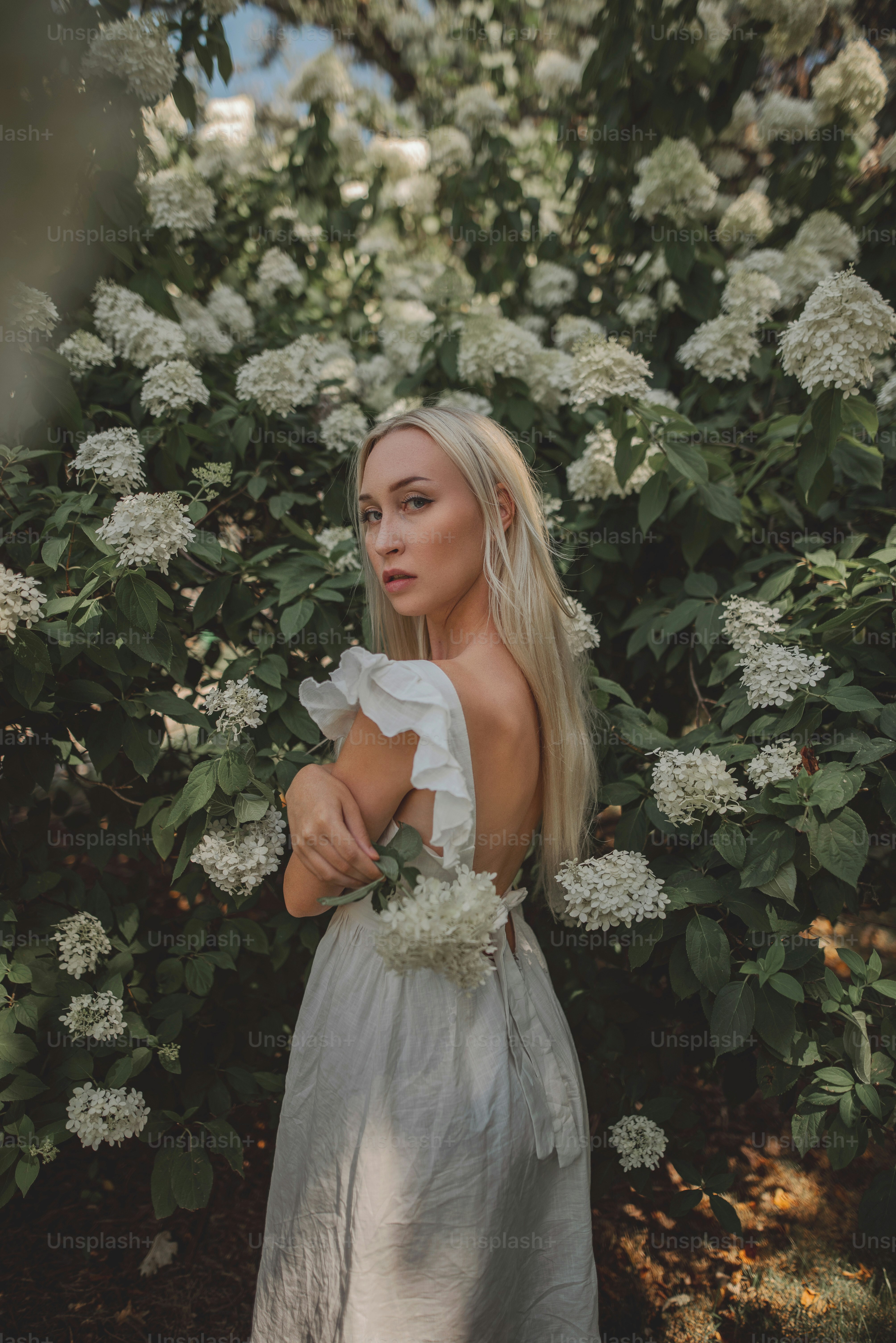 Une femme en robe blanche debout devant un buisson