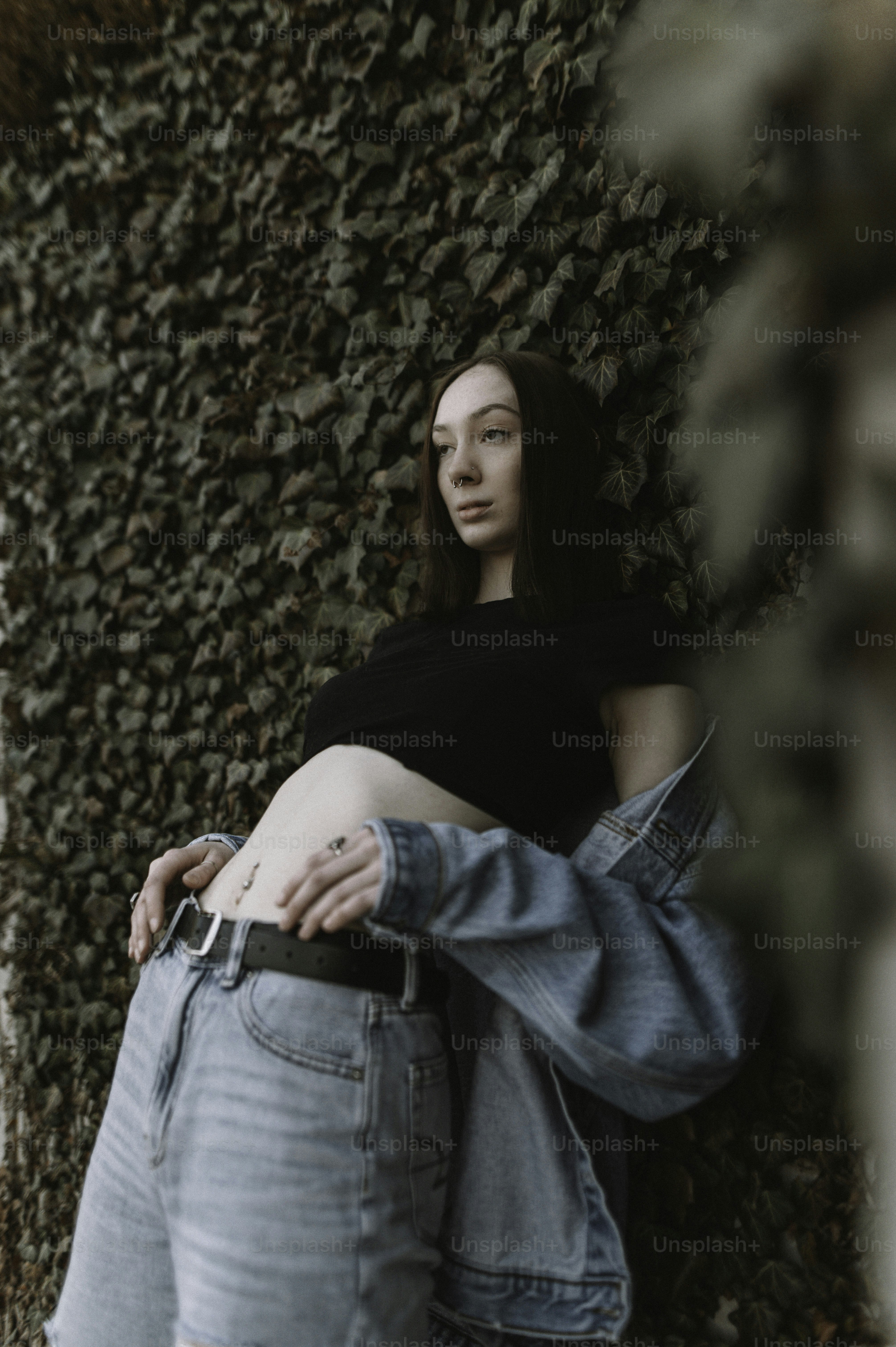 a pregnant woman leaning against a wall covered in ivy